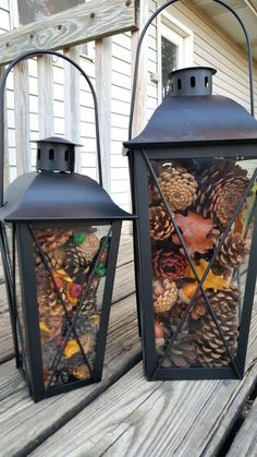 two black lanterns filled with pine cones and acorns sitting on a wooden porch