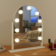 a mirror that has lights on it in front of a desk with a laptop and other items