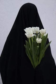 a woman wearing a black shawl holding white tulips