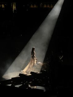 a woman in a white dress standing on stage with light streaming through her head and hands behind her back