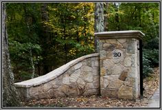 a stone gate with a number on it in front of some trees and leaves at the park