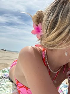 a woman sitting on top of a beach next to the ocean with a pink flower in her hair