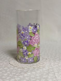 a glass with flowers painted on it sitting on a lace doily covered tablecloth