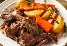 a white plate topped with roast, potatoes and carrots