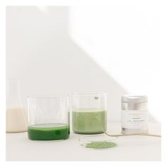 three glasses with green liquid next to each other on a white surface, one containing a powder and the other containing an ointment