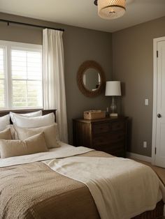 a bed sitting under a window next to a lamp and dresser in a room with white curtains