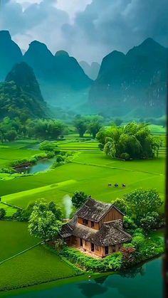 an aerial view of a house in the middle of a green field with mountains behind it