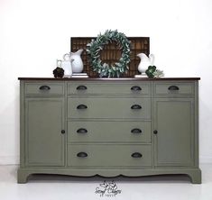 a green dresser with two vases and a wreath on top