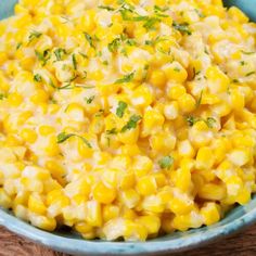 a blue bowl filled with corn on top of a wooden table and garnished with parsley