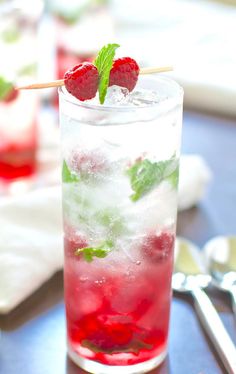 a glass filled with ice and raspberries sitting on top of a blue table