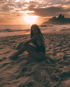 a woman sitting on top of a sandy beach next to the ocean under a cloudy sky