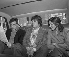 three people sitting in the back seat of a car looking at something on a paper