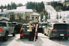 a man standing in the snow with his skis next to some cars and a building