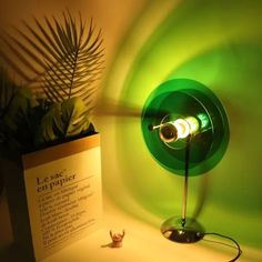 a green lamp sitting on top of a table next to a plant and a sign