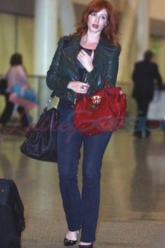 a woman with red hair is walking through an airport carrying her purse and looking at the camera