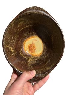 a hand is holding a brown bowl with something in the bottom and yellow substance inside