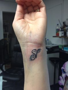 a hand holding up a small tattoo with the letter s on it's wrist