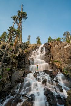 a man standing on top of a waterfall in the middle of a rocky mountain range