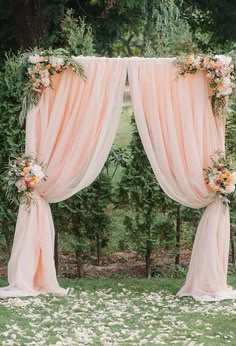 an outdoor wedding ceremony setup with pink drapes and flowers on the grass, surrounded by greenery