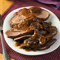 a white plate topped with meat covered in gravy next to a fork and knife