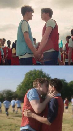 two men in red and blue shirts holding hands, one is kissing the other's forehead