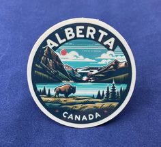 a sticker that says alberta in front of a mountain and lake with a bison