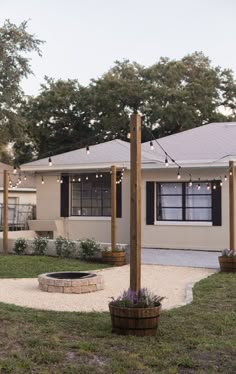 a house with lights strung from the roof and trees in the front yard, next to a fire pit