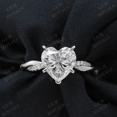 a heart shaped diamond ring on top of a black satin material with diamonds around it