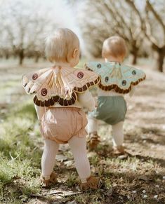 two toddlers are walking in the grass and one is wearing a butterfly wings top