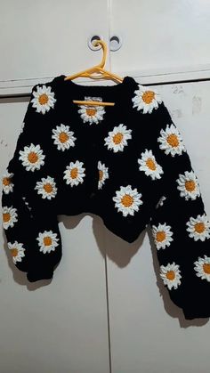 a black sweater with white and yellow flowers on it hanging from a wooden hanger