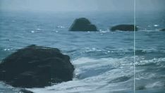 two large rocks in the ocean with waves coming up on them and one rock sticking out of the water