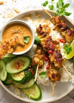 chicken skewers with cucumbers, rice and sauce on a white plate