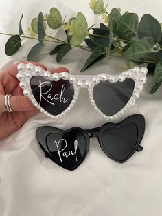 two heart shaped sunglasses with the words rach and paul written on them, one being held by a woman's hand