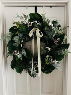 a wreath with pine cones and greenery hangs on the front door