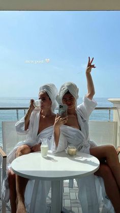 two women sitting at a table with towels on their heads, taking a selfie