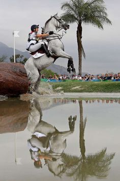 a man riding on the back of a white horse next to a body of water