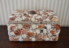 a decorative box made out of seashells sits on a table next to a striped wall