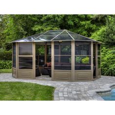 a gazebo in the middle of a yard with a pool and trees behind it