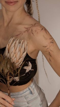 a woman wearing a crop top and holding a flower in her right hand with two birds on it