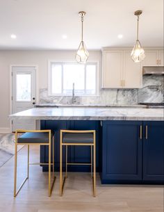 a kitchen with marble counter tops and blue cabinets, two stools in front of the island