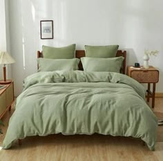 a bed with green sheets and pillows in a white room next to a lamp on a table