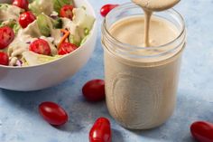 a bowl of salad with dressing being poured into it and cherry tomatoes on the side