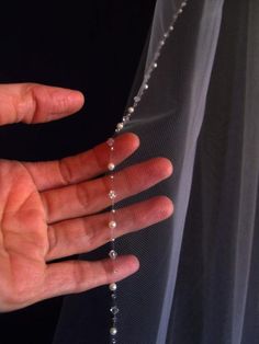 a person's hand with a beaded necklace on their left and a veil on the right