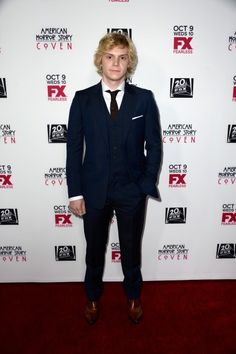 a young man in a suit and tie standing on a red carpet at an event