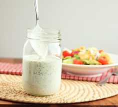 a glass jar filled with food sitting on top of a table next to a bowl of salad