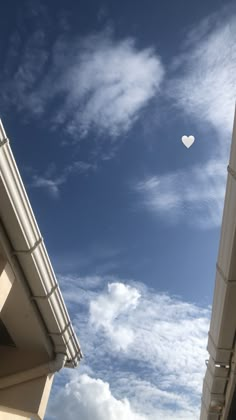 a white heart shaped balloon flying in the sky above some buildings on a sunny day