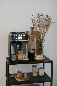 a coffee machine sitting on top of a black shelf next to cups and vases