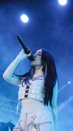 a woman in white outfit holding a microphone up to her mouth while standing on stage