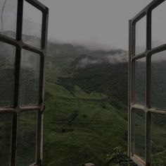 an open window looking out onto a green valley and mountains in the distance with fog