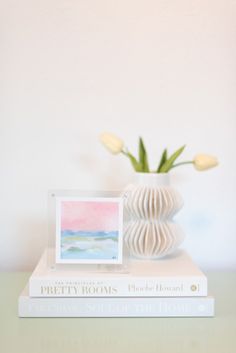 a white vase with yellow tulips on top of two books and a photo frame